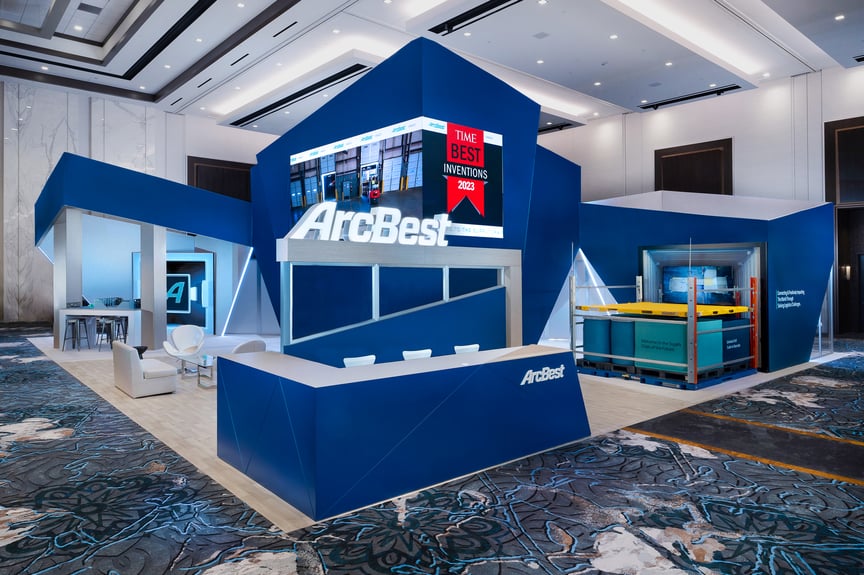 Modern, blue trade show booth with the ArcBest logo prominently displayed. A large screen features the text "Time's Best Inventions 2023. Modern, blue trade show booth with the ArcBest logo prominently displayed. A large screen features the text "Time's Best Inventions 2023.